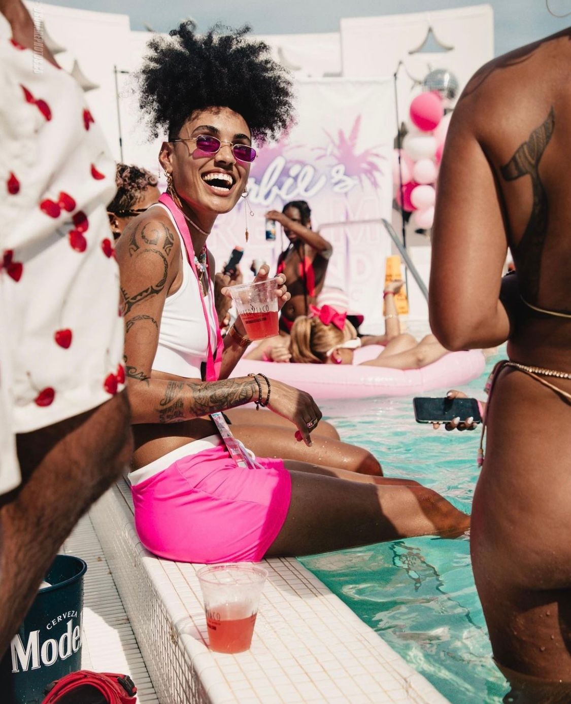 Summer pool party scene with attendee in pink swimwear laughing by the water.