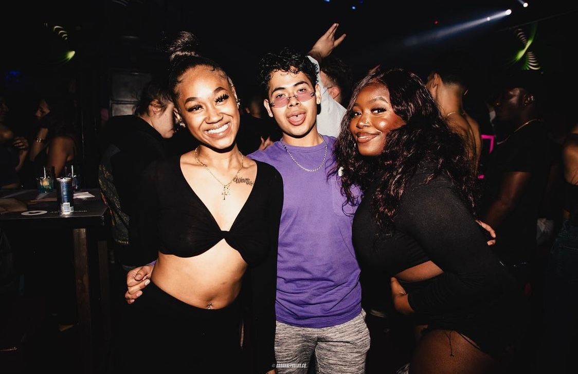 Three partygoers pose enthusiastically at a dark nightclub.