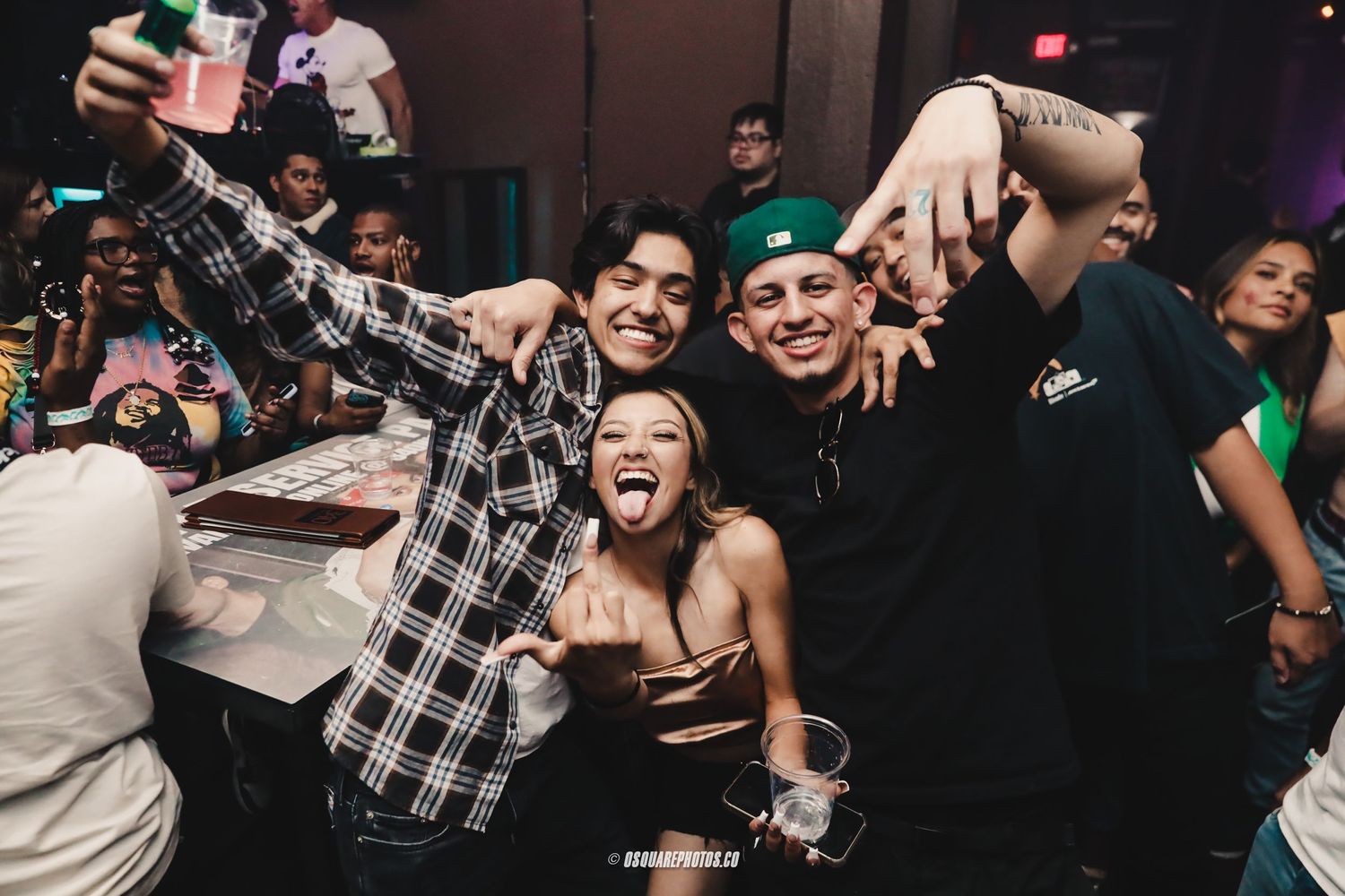 Group of energetic partygoers taking selfies and celebrating at a crowded nightclub.