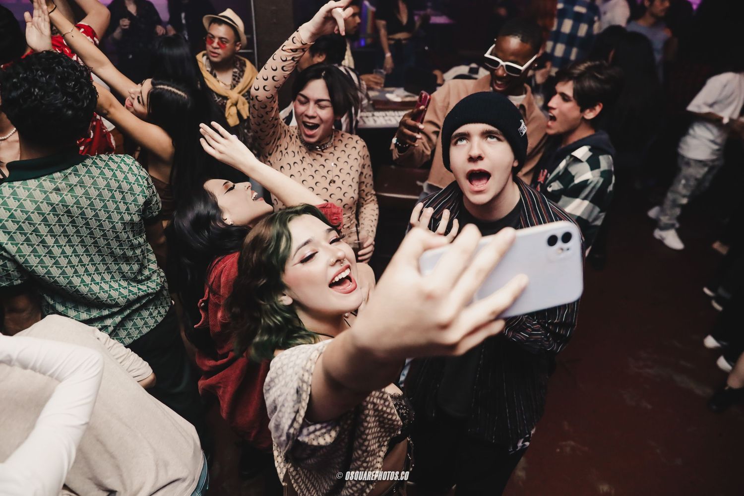 Energetic crowd taking selfies and dancing at a lively nightclub party.