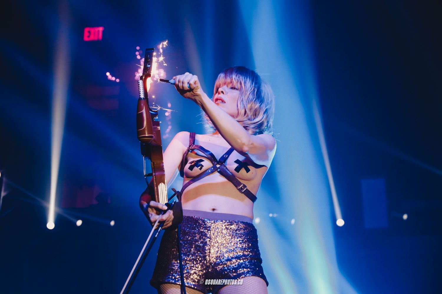 Performer in sparkly outfit playing violin on stage with dramatic blue lighting and spotlights.