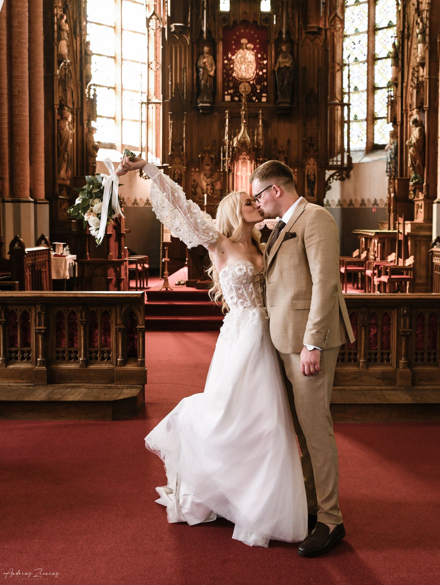 Newlyweds share an intimate moment in an ornate church with gothic architecture and red carpet.