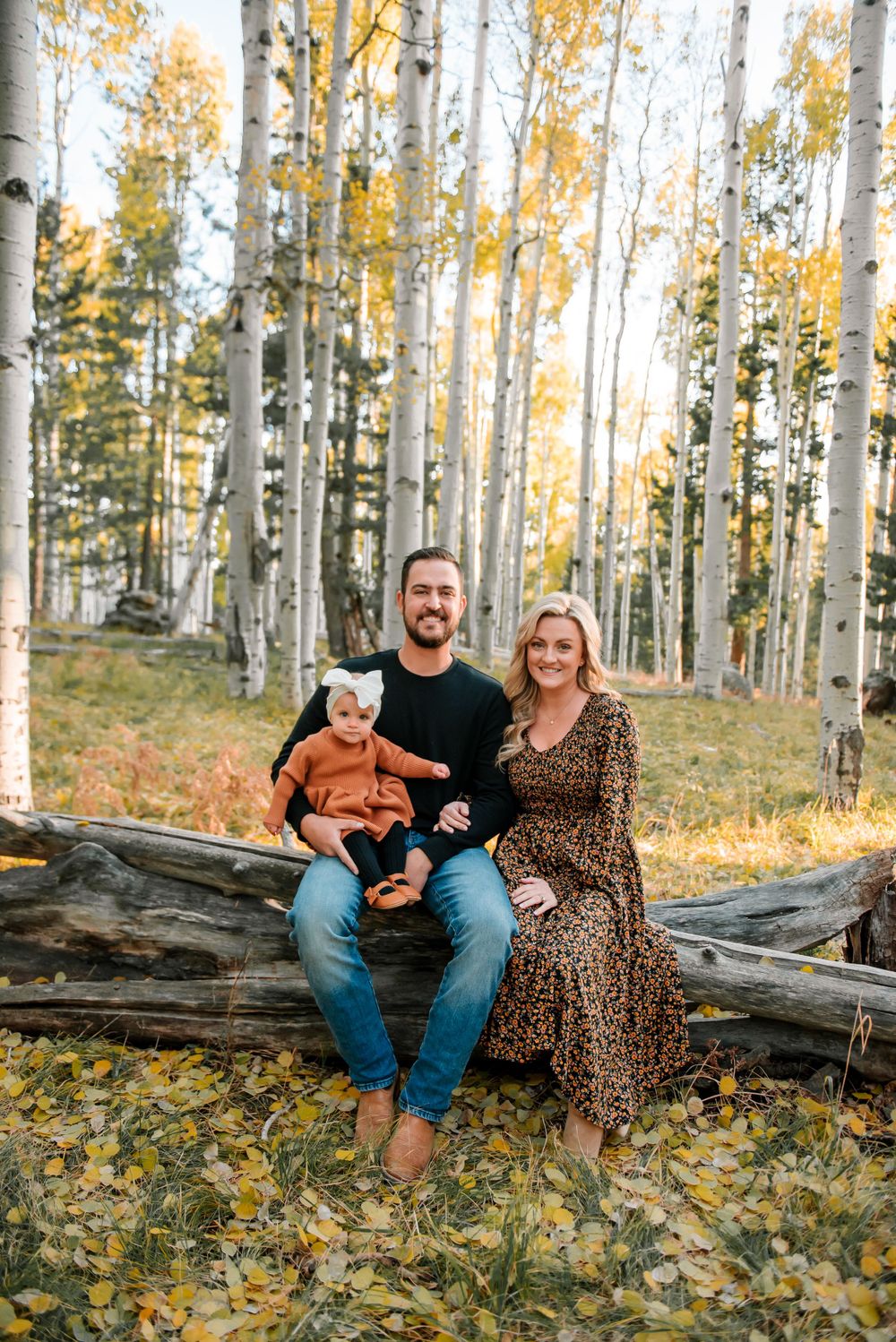 Family relaxing on fallen log surrounded by golden aspen trees in autumn.