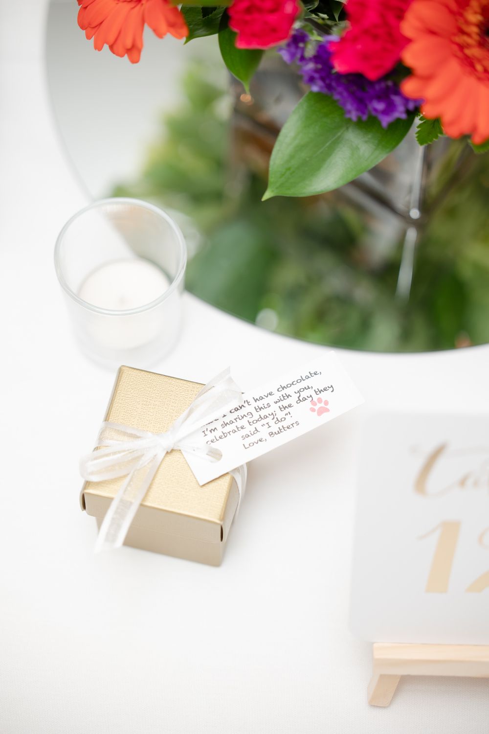 Small gift box with handwritten note next to colorful floral arrangement.