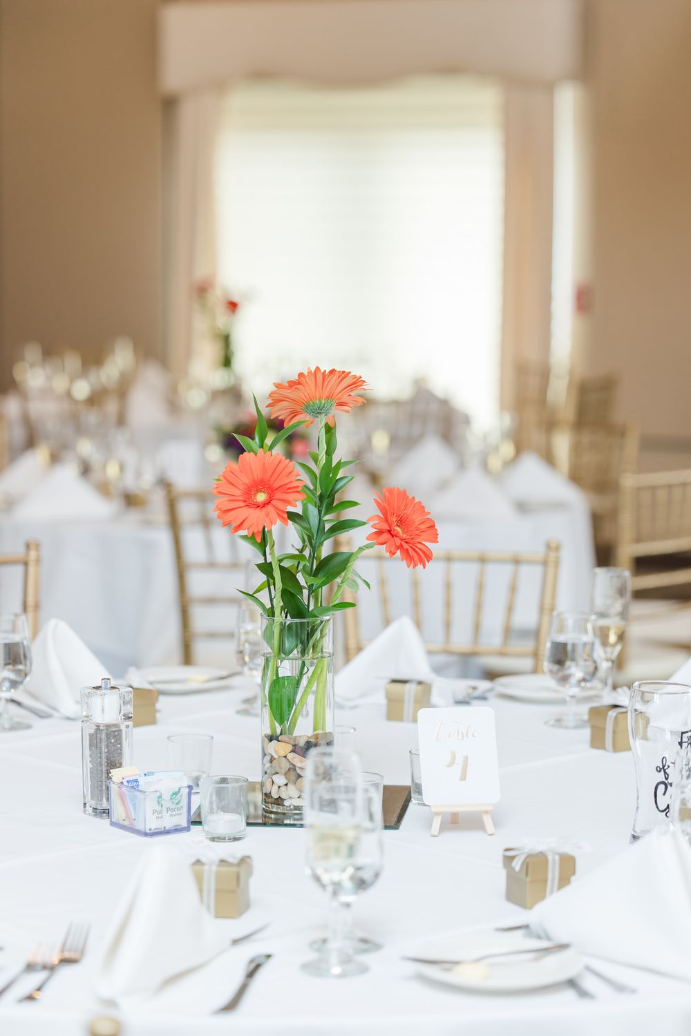 Wedding reception table with coral gerbera daisy centerpiece and gold favor boxes.