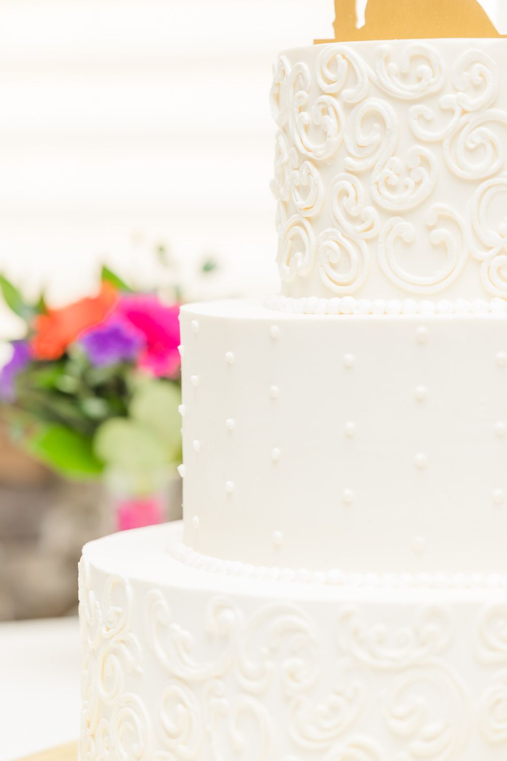 Elegant white wedding cake with swirled pattern detail and bright floral accents.