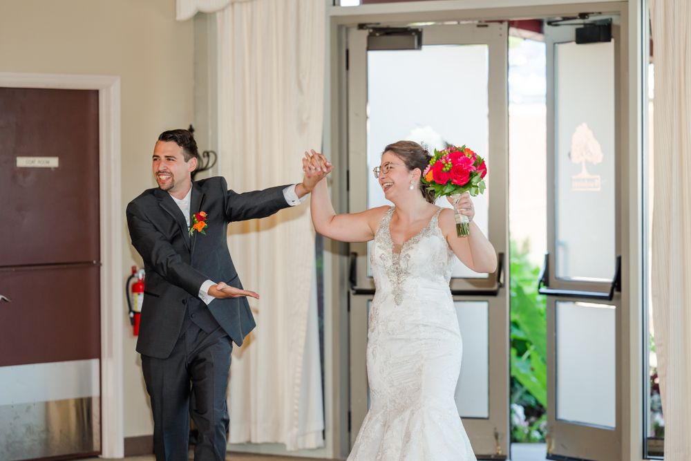 Wedding couple makes dramatic entrance with playful poses and bright bouquet.