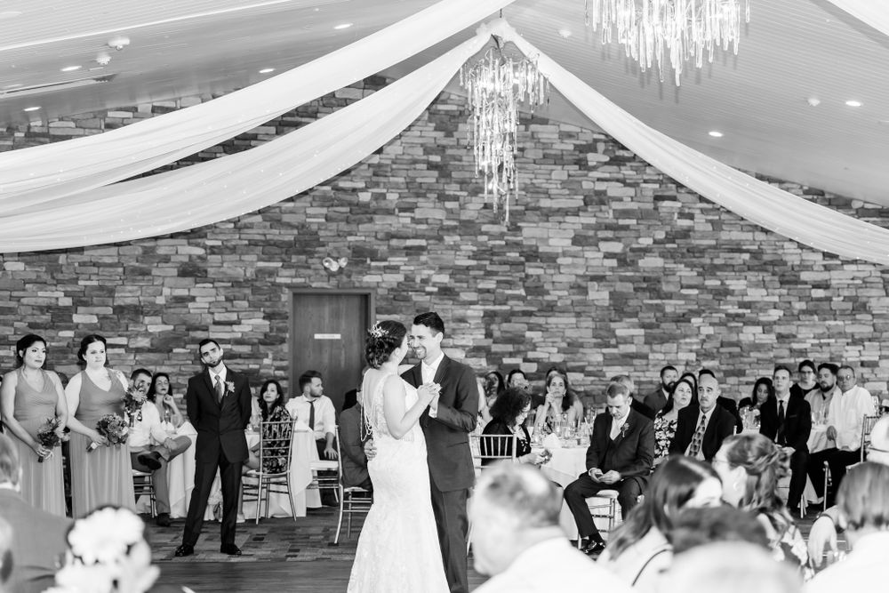 Couple sharing their first dance at a wedding reception with white drapes and stone wall backdrop.