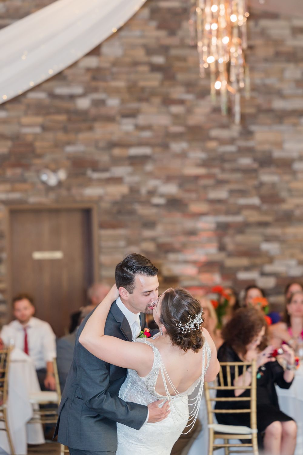 Couple dancing under elegant chandelier lighting and draped fabric at wedding reception.