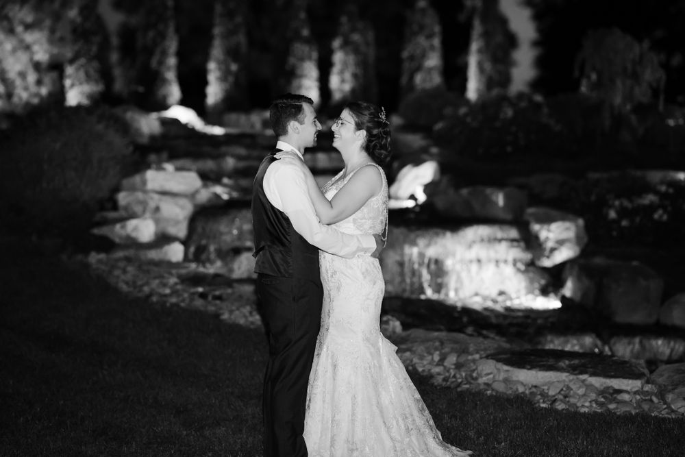 Black and white romantic portrait of couple embracing outdoors by illuminated stone wall.