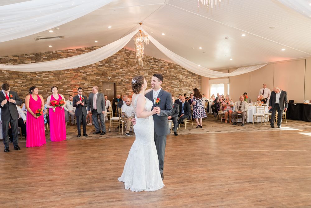 First dance at wedding reception with draped fabric decor and pink bridesmaid dresses visible.
