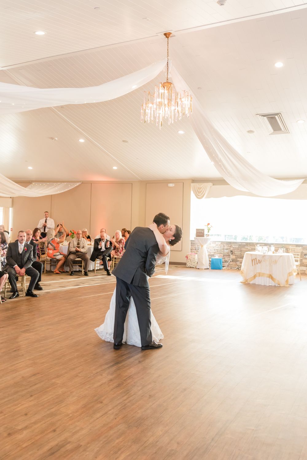 Elegant ballroom dance under crystal chandelier and white fabric draping.