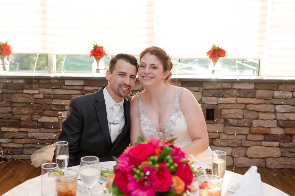 Newlyweds share laughter at their reception table decorated with bright pink flowers.