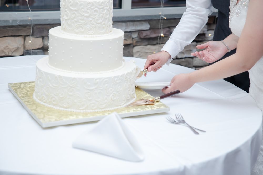 Close up of white tiered wedding cake being cut on table.