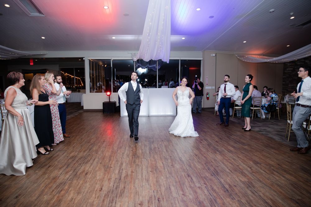Wedding celebration on wooden dance floor with colored lighting and white drapery.