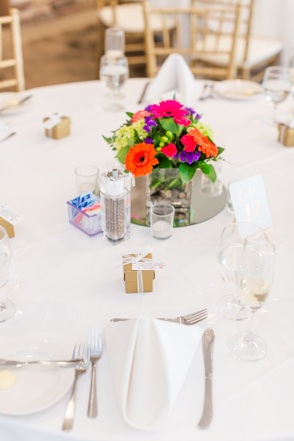Elegant wedding table setting with vibrant floral centerpiece, white linens, and small gift boxes.