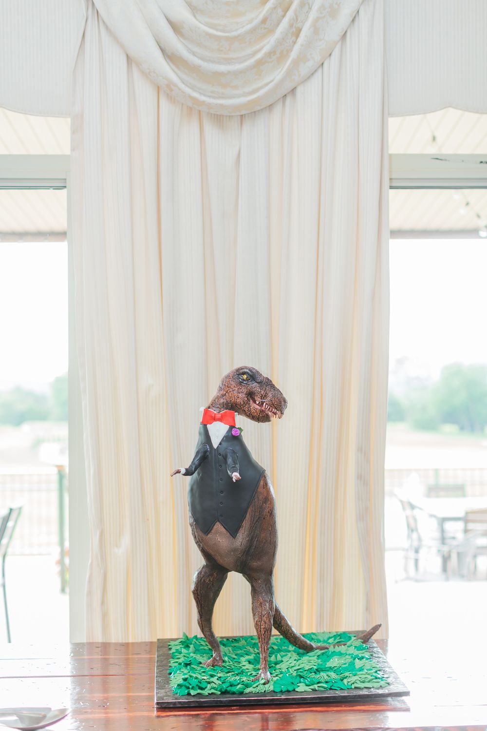Whimsical groom's cake featuring a brown dog sculpture wearing a bow tie on green grass.