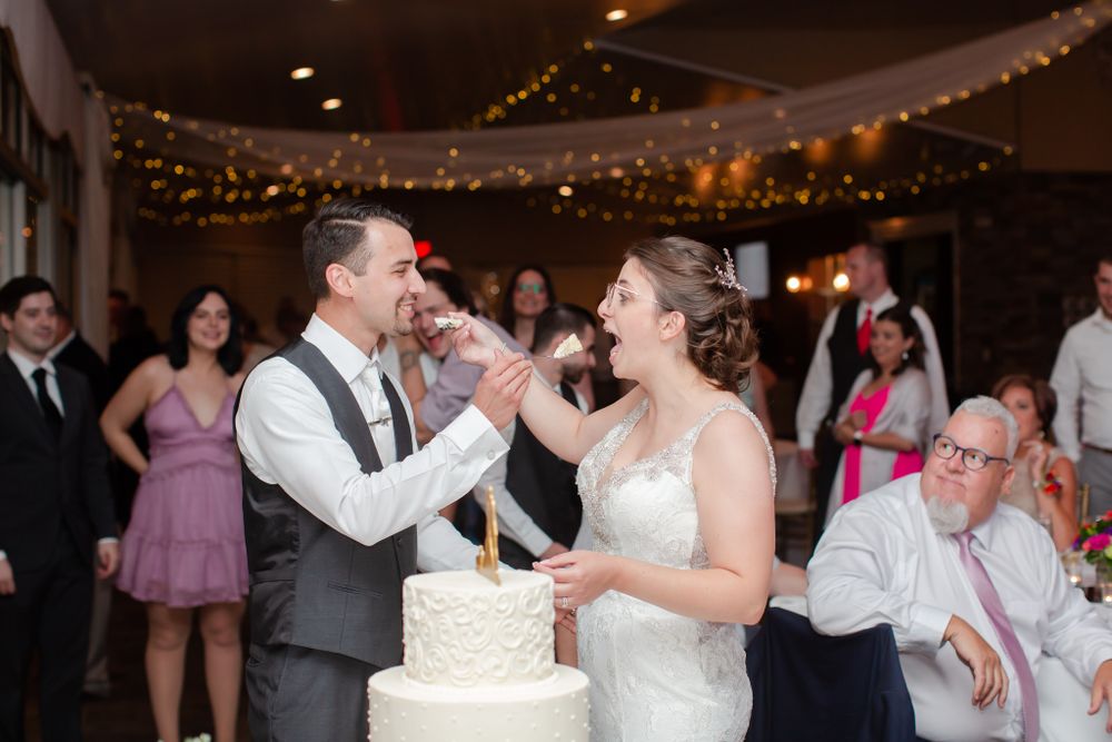 Traditional cake cutting moment at wedding reception with decorative string lights in background.