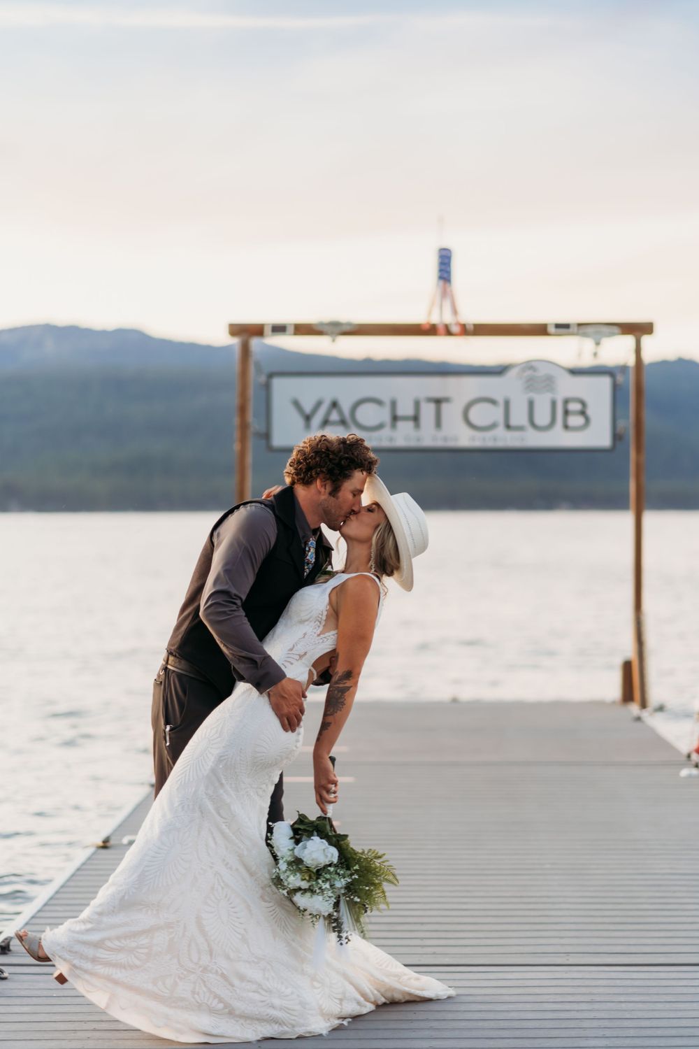 Romantic moment on a dock with Yacht Club sign and mountains in background.