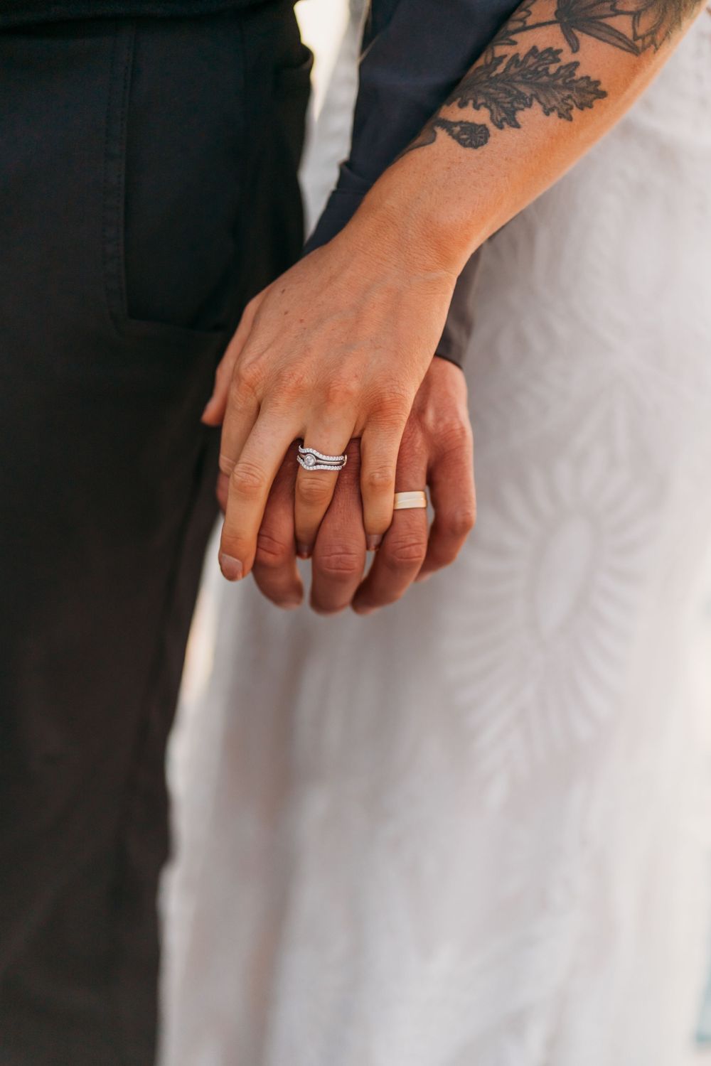 Close-up of tattooed hands with wedding rings against black and white formal attire.