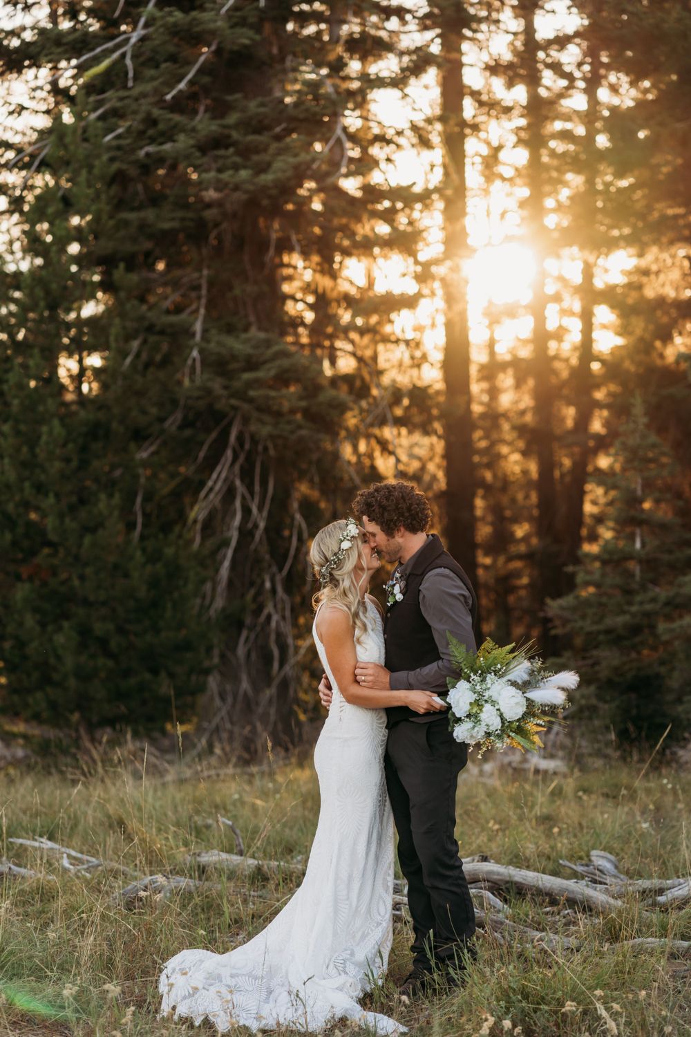 Romantic wedding couple embrace in golden forest light with white floral bouquet.