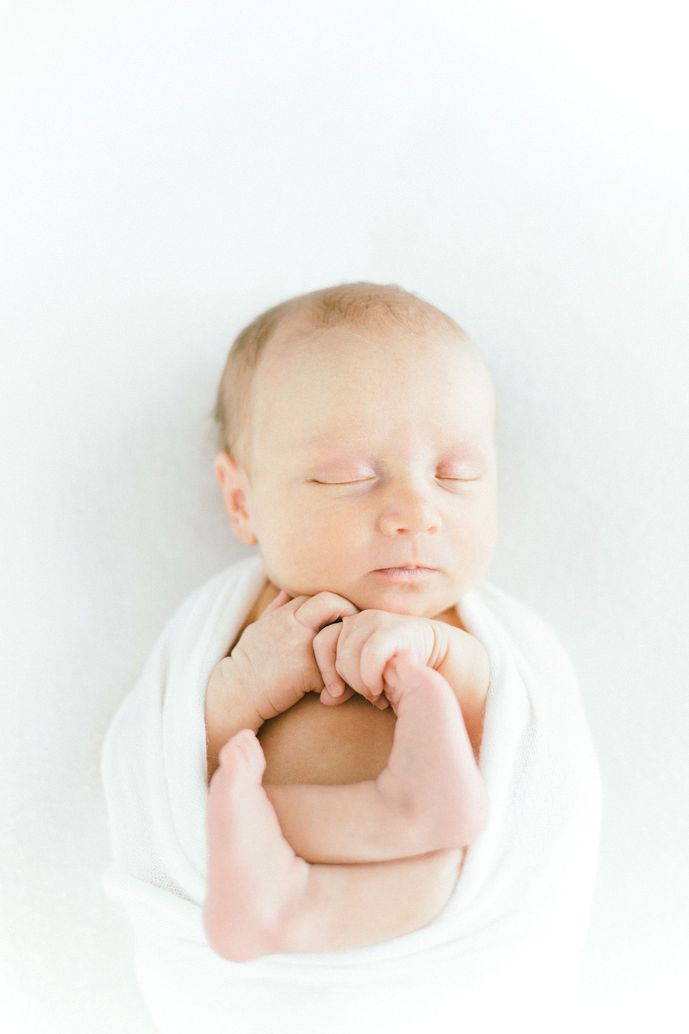 Serene newborn portrait with baby's hand near face on white background.
