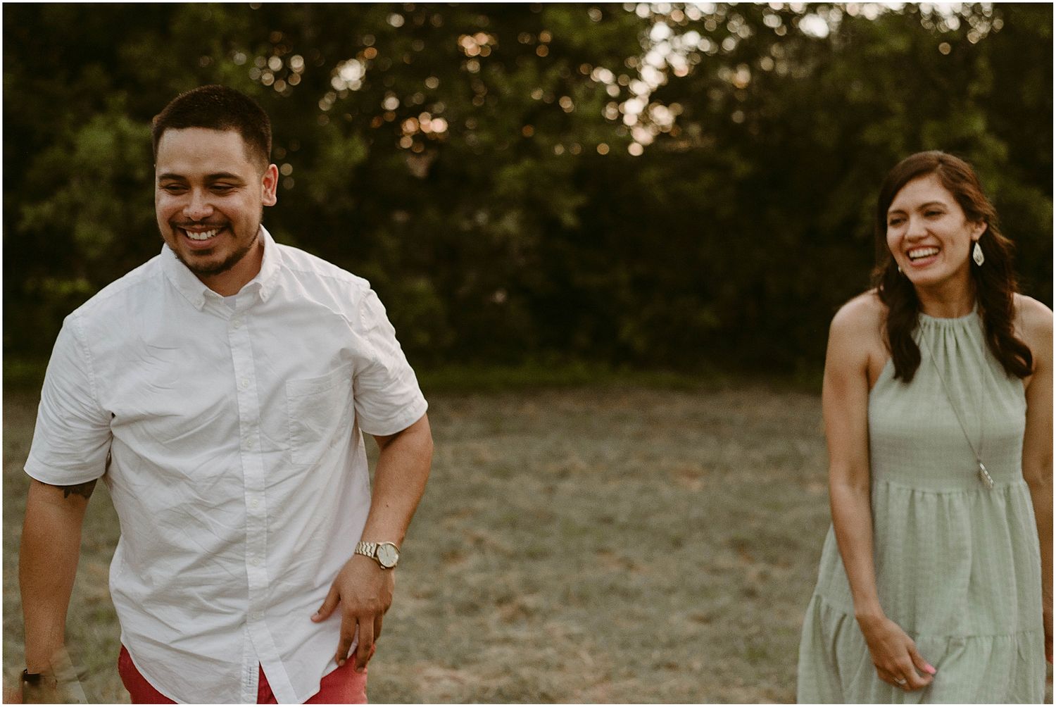 A joyful couple sharing candid laughter in a field during golden hour.