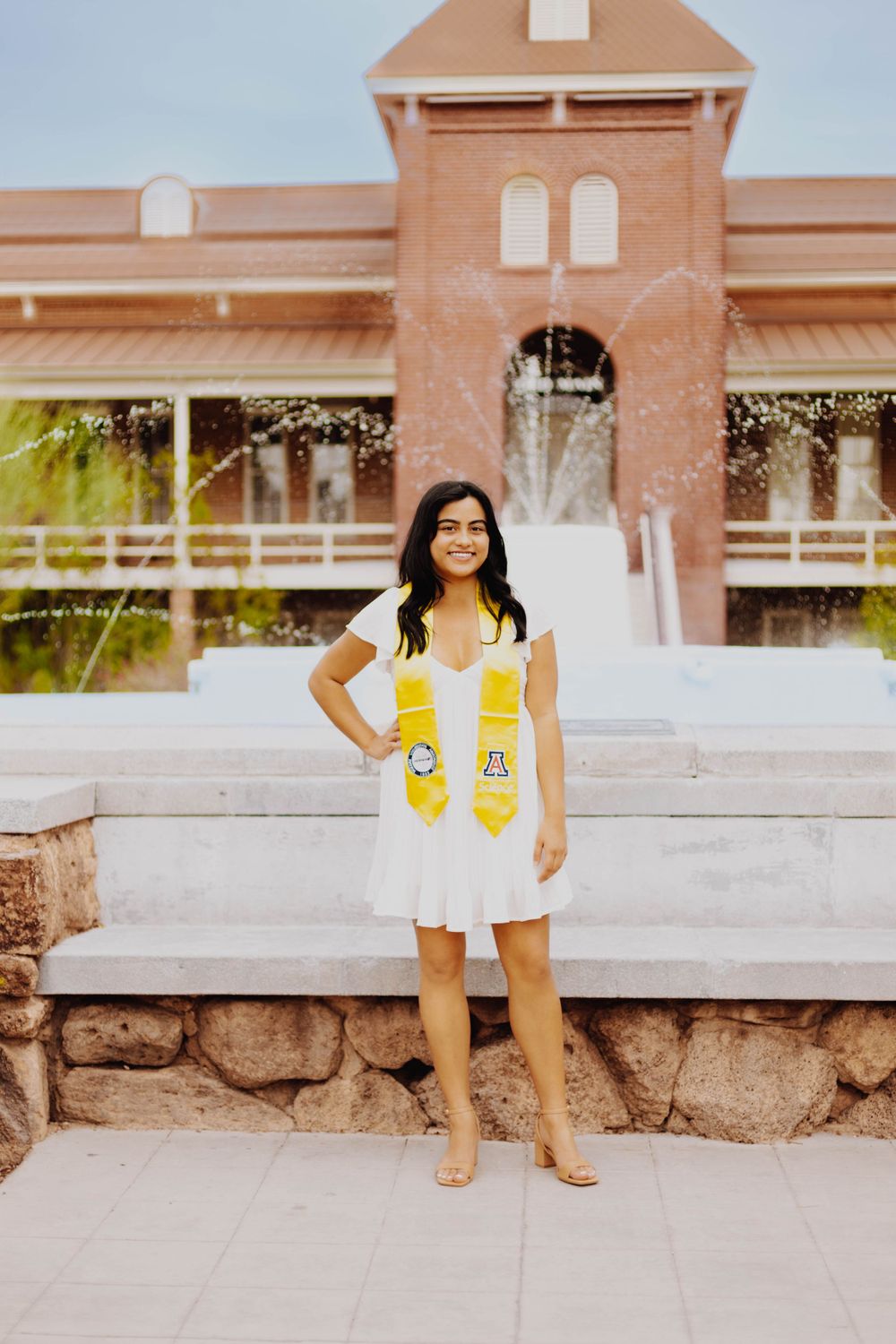 Senior portrait sitting on stone ledge wearing bright yellow stole.