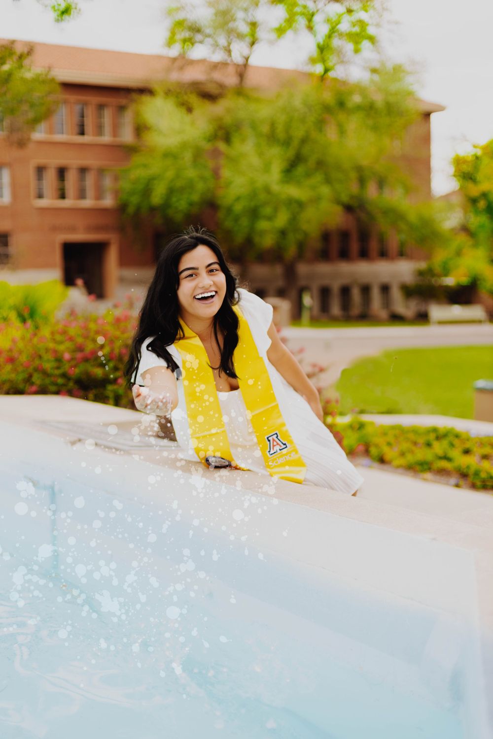 Joyful graduation photo shoot near fountain with yellow academic stoles.