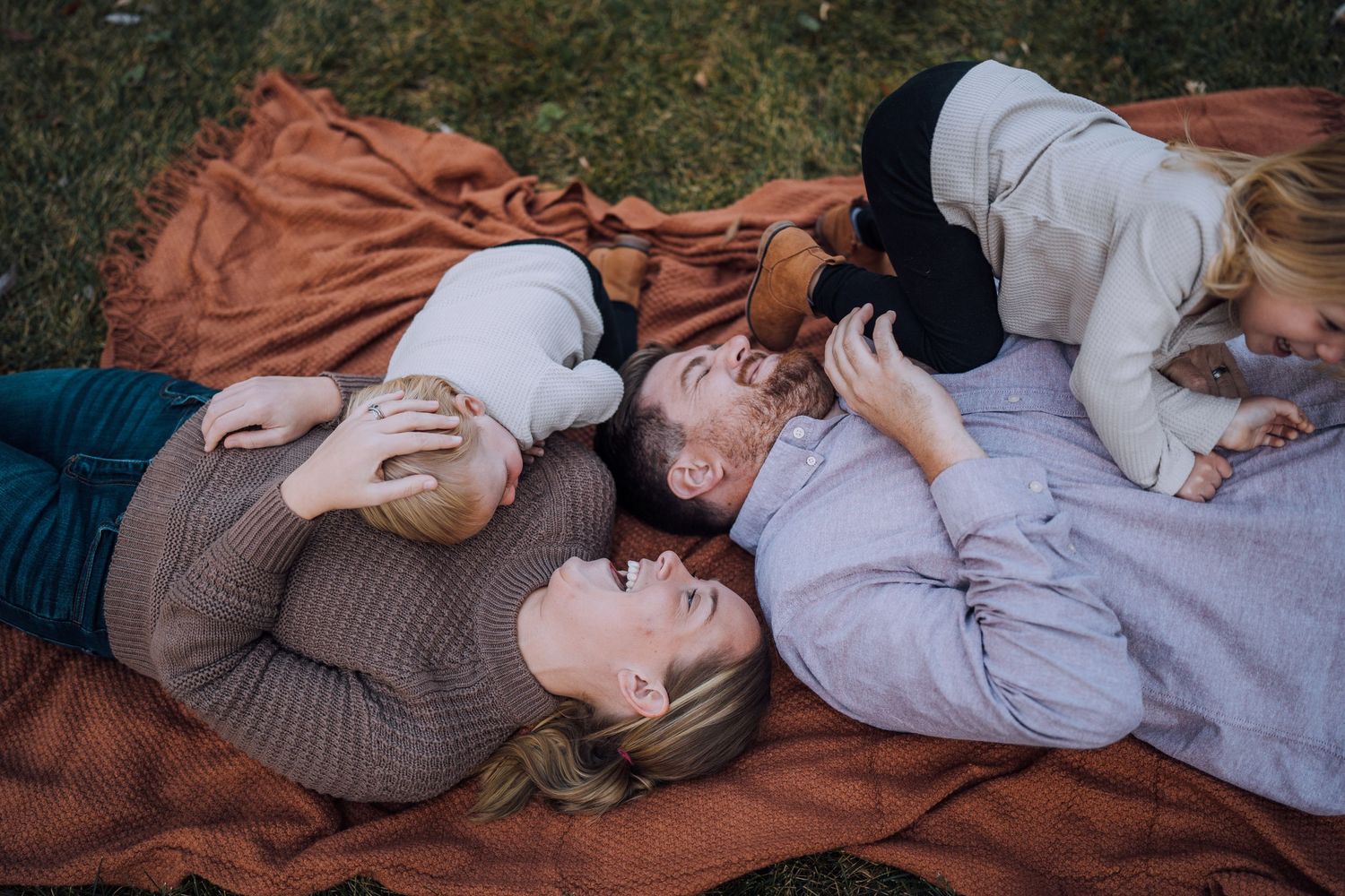 A family shares intimate moments while lying together on a autumn blanket outdoors.