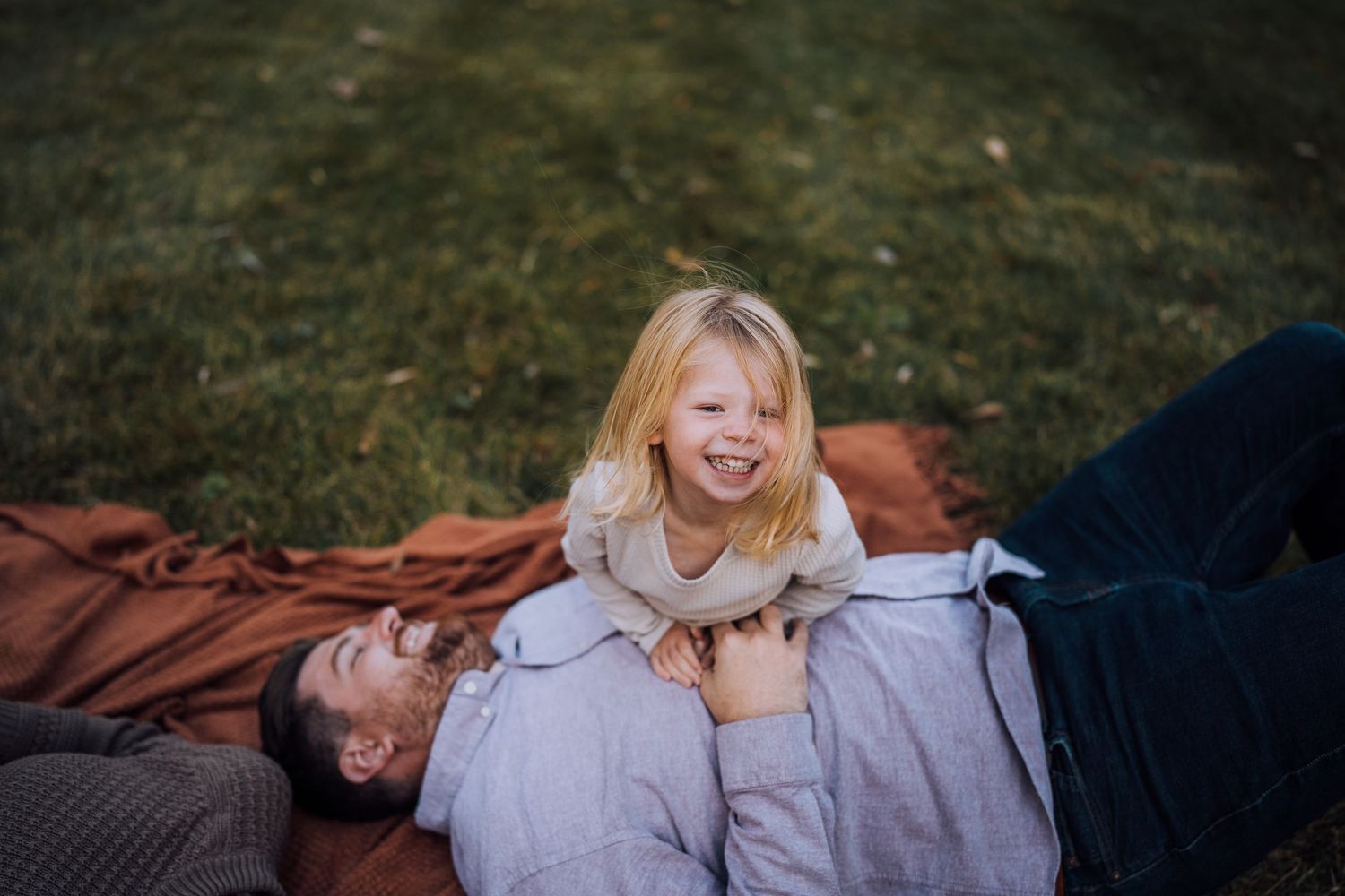 Candid laughter shared between family members while relaxing on a blanket outside.