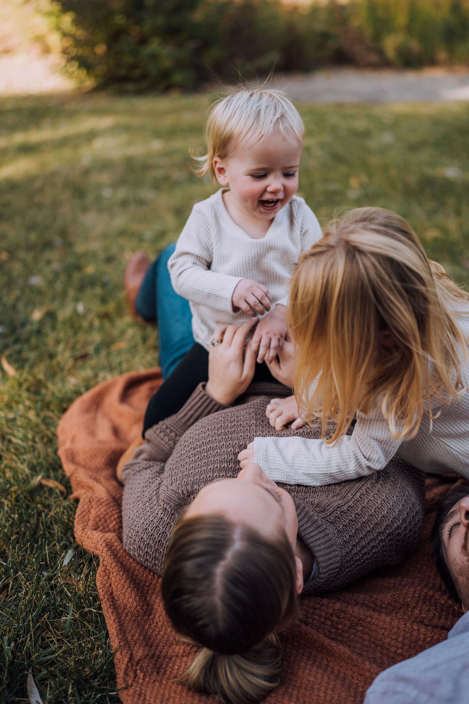 Playful family moments captured on a cozy blanket during an outdoor photo session.