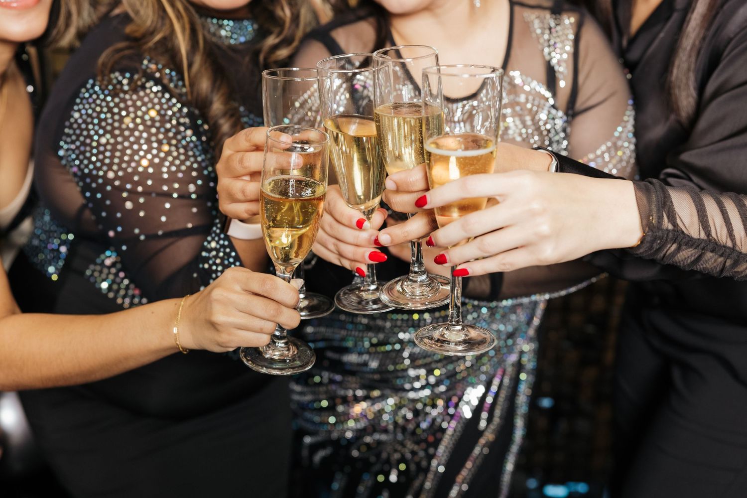 Friends in sparkly dresses toasting with champagne glasses at celebration.