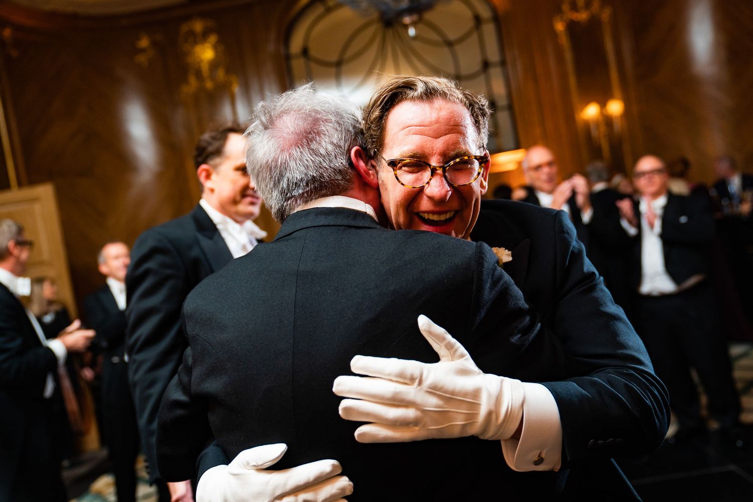 Unposed photograph of two men hugging during Claridges Hotel wedding celebrations