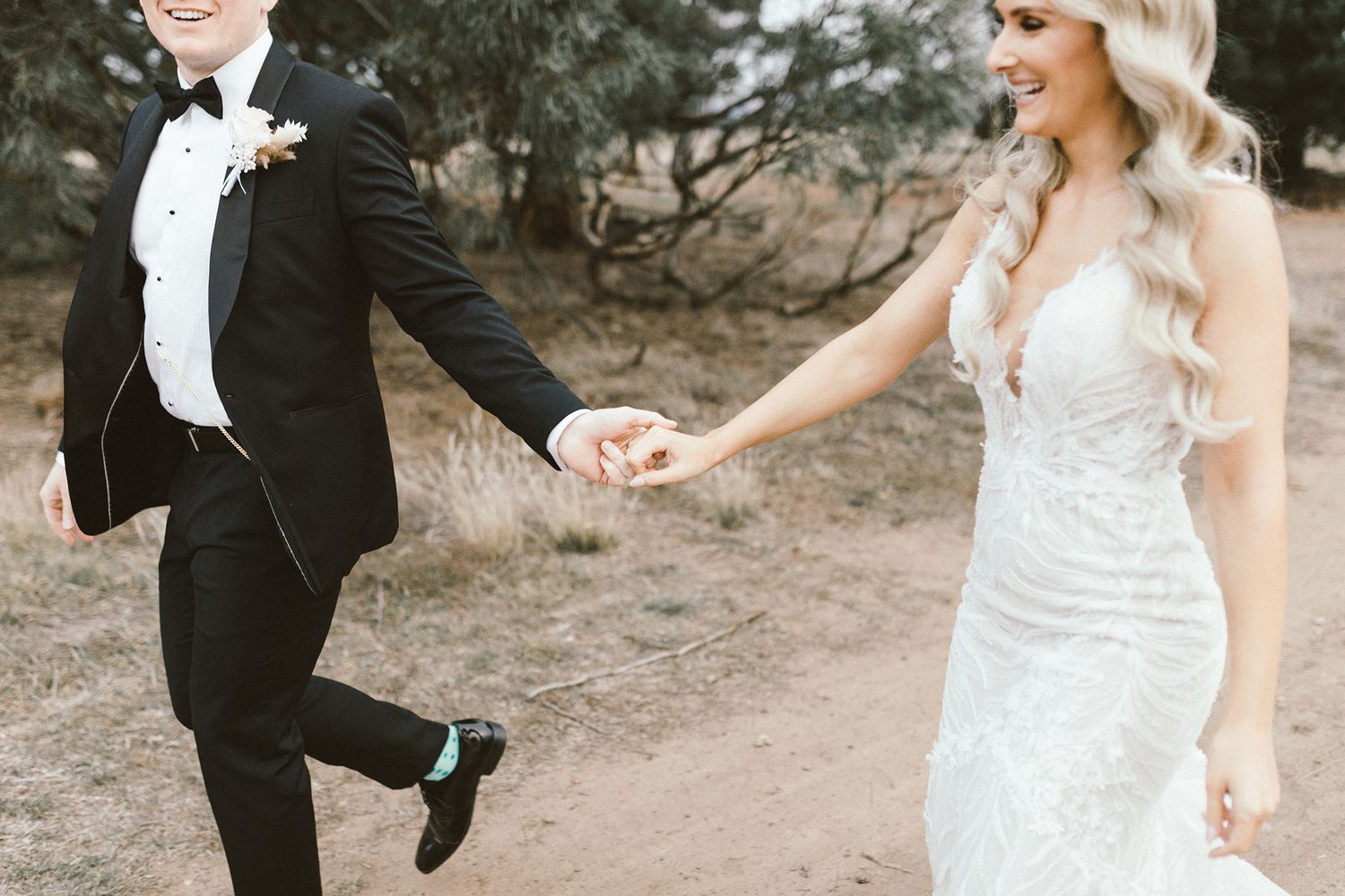 A playful wedding moment as couple walks hand in hand on a dirt path.