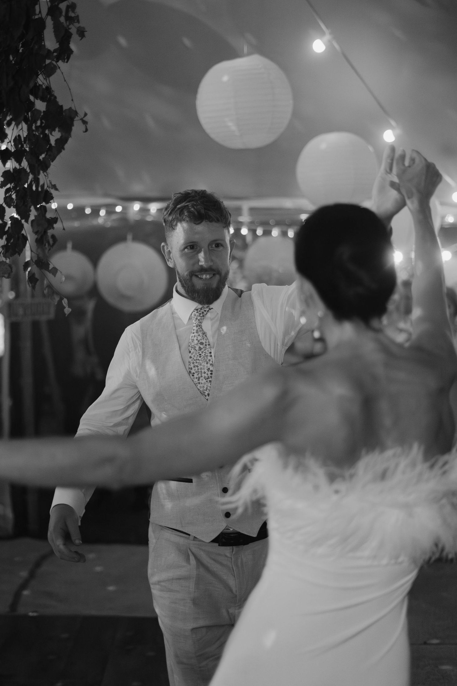 groom twirling bride underneath fairy lights and lanterns during first dance in marquee in oxfordshire
