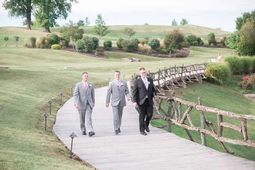 Wedding party walks down a curved pathway surrounded by green landscaping and rustic wooden fencing.