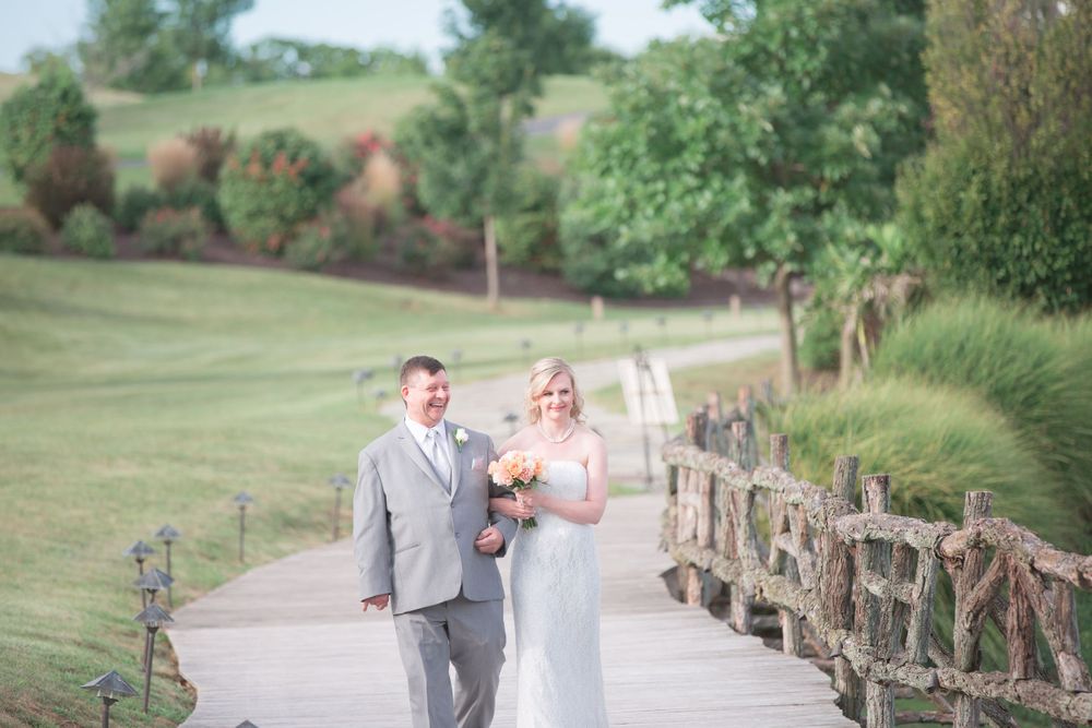A wedding couple strolls along a winding path with rustic wooden railings on a lush golf course.