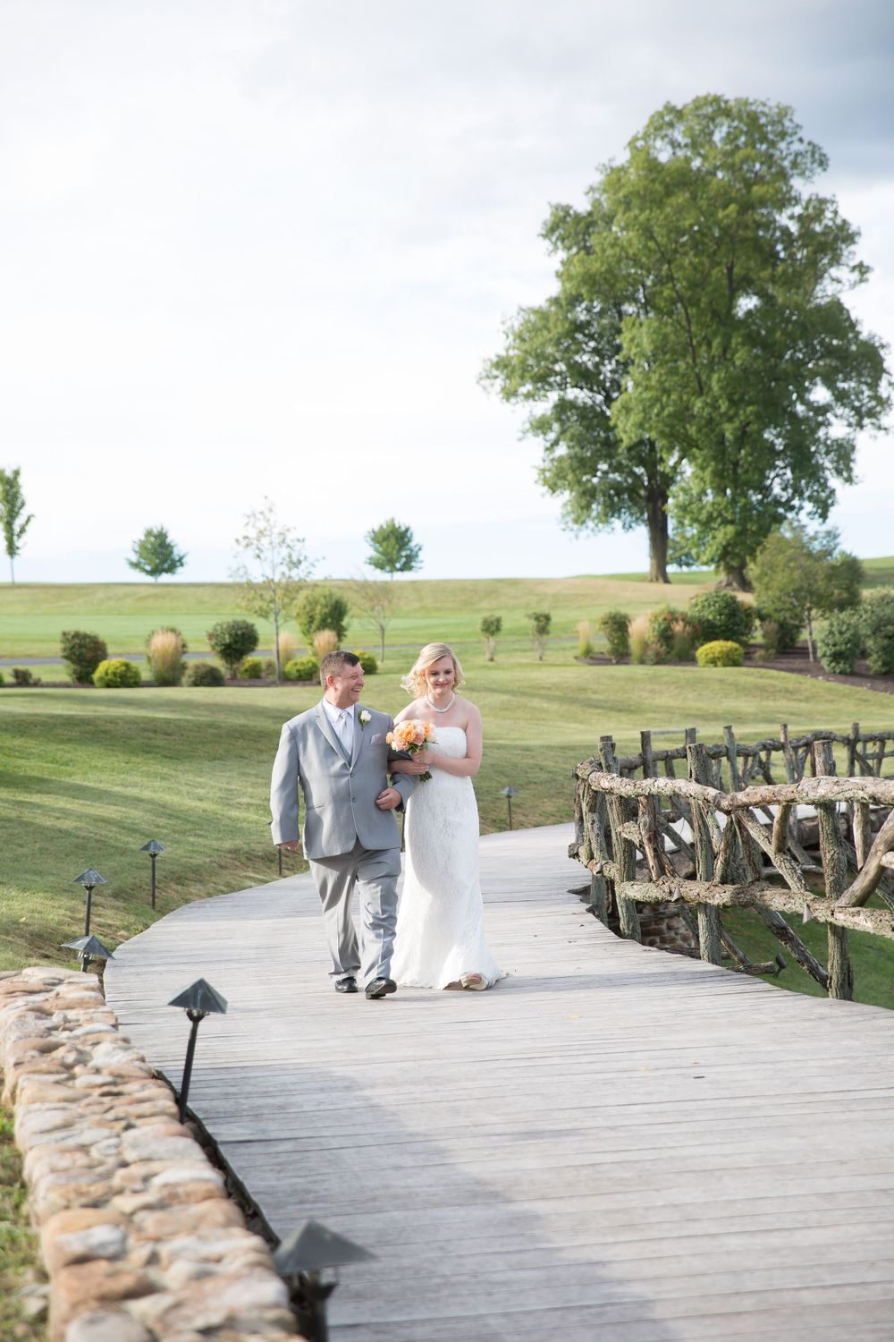 Couple walks along curved wooden boardwalk through manicured golf course landscape.