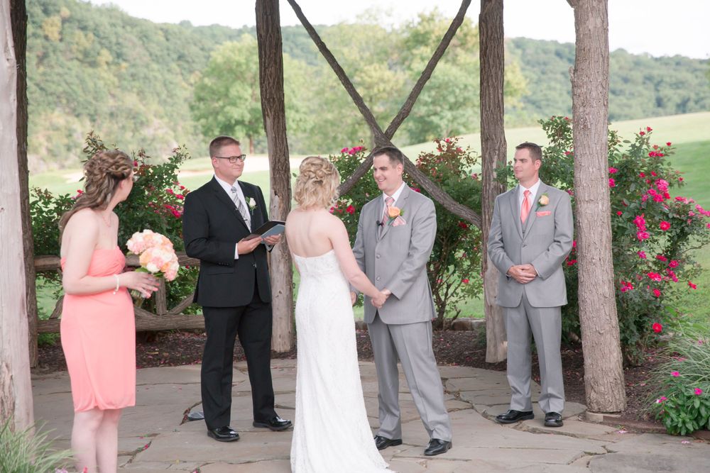 Outdoor wedding ceremony with bridal party gathered under rustic wooden pavilion.