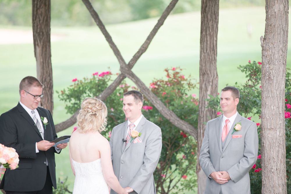 Wedding officiant conducts ceremony for couple under wooden pergola with floral accents.