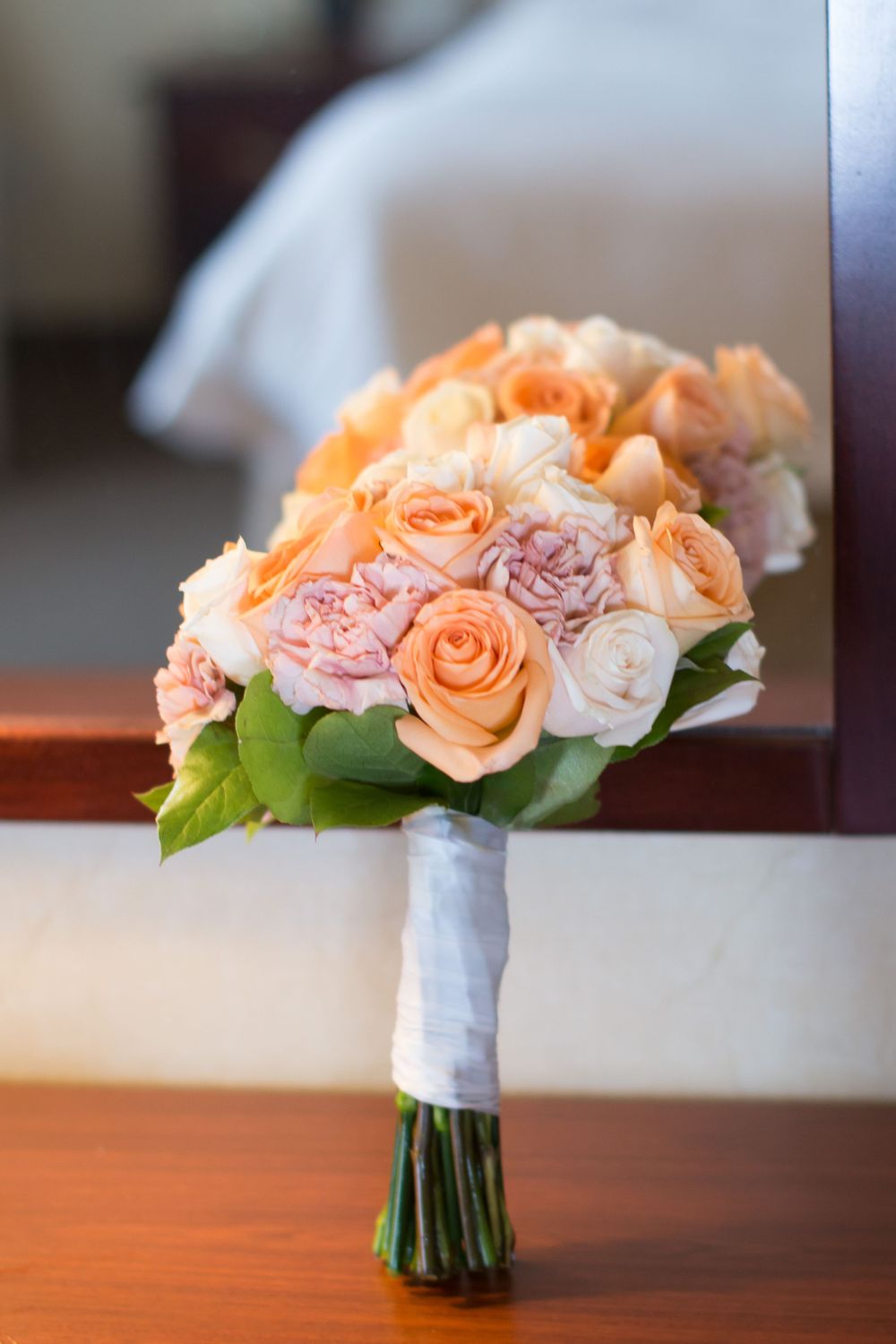 Beautiful peach and pink rose wedding bouquet wrapped in white ribbon.