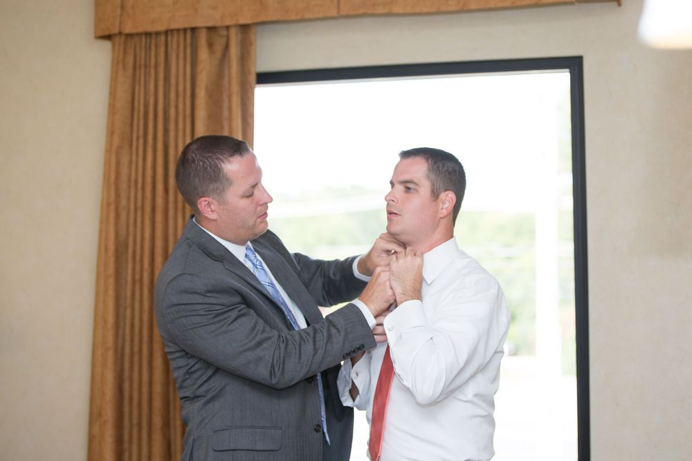 Two men in formal attire adjusting a tie before an event.