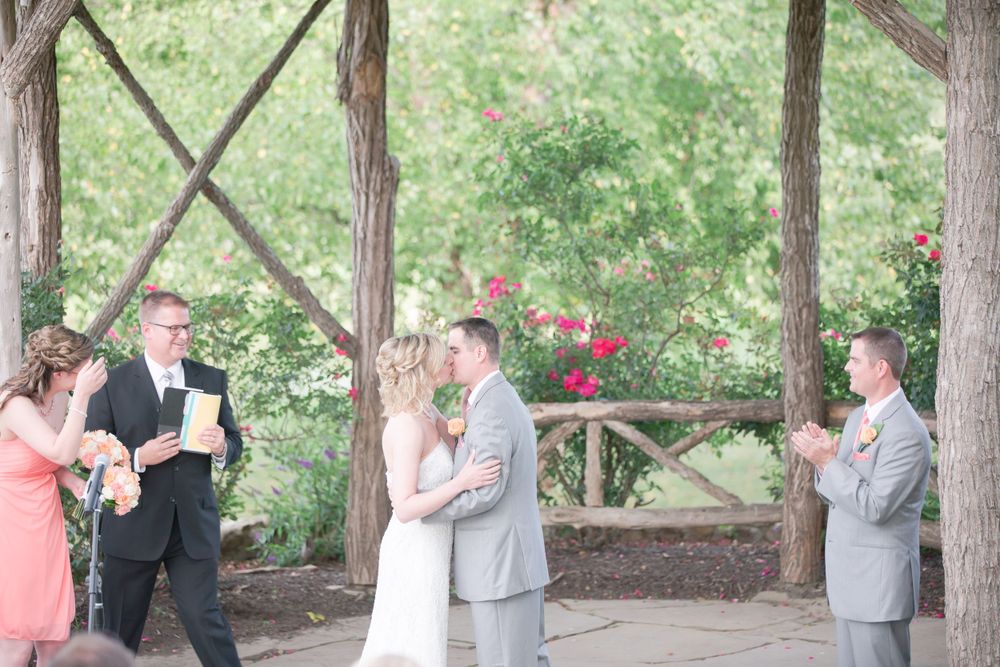 Wedding ceremony guests gather under a wooden gazebo decorated with red roses.