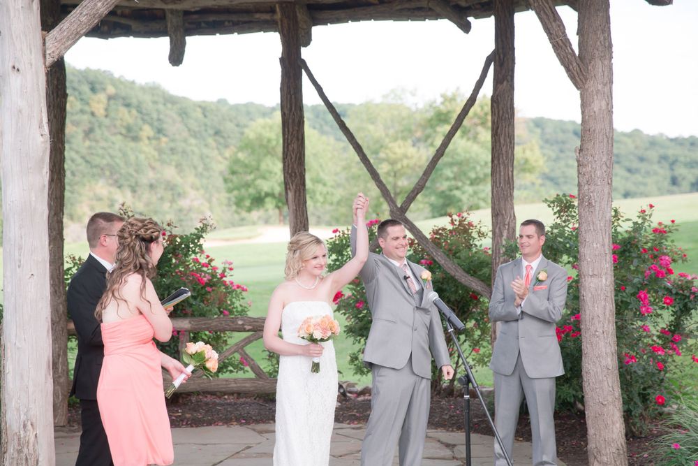 Wedding ceremony taking place under a rustic wooden pavilion with climbing roses.