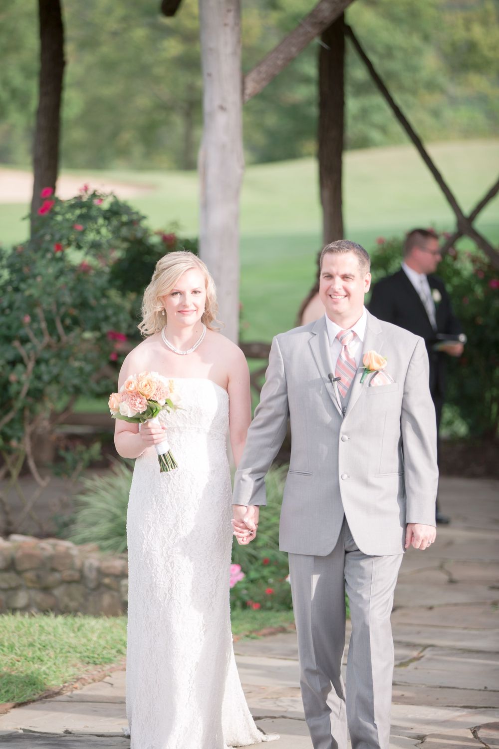 A couple in wedding attire walks along a stone path surrounded by garden landscaping.