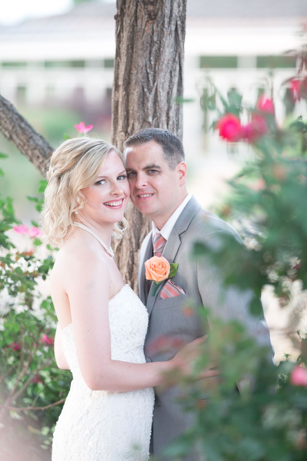 Romantic wedding portrait with couple among pink flowering bushes and rustic tree trunk.