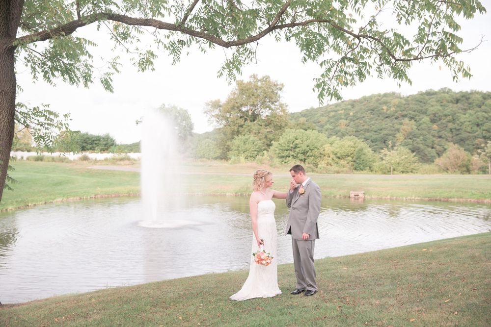 Newlyweds pose for photo by lake with water fountain spraying in background.