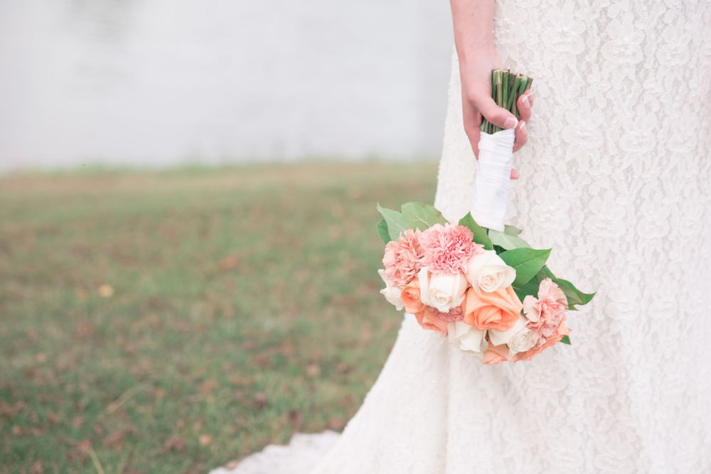 Close-up of peach and pink bridal bouquet with roses against white wedding dress.