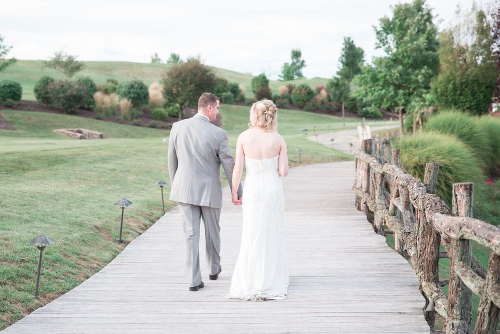 A couple strolls along a wooden walkway surrounded by lush green countryside.